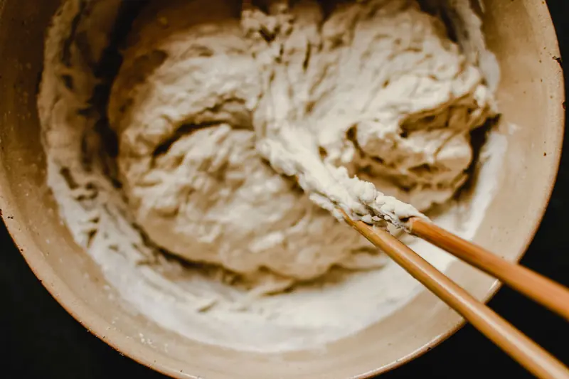 Close-up view of dough being mixed in a bowl using chopsticks, evoking a rustic kitchen feel