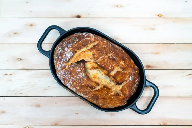 Top view of a homemade sourdough loaf in a Dutch oven, resting on a wooden surface