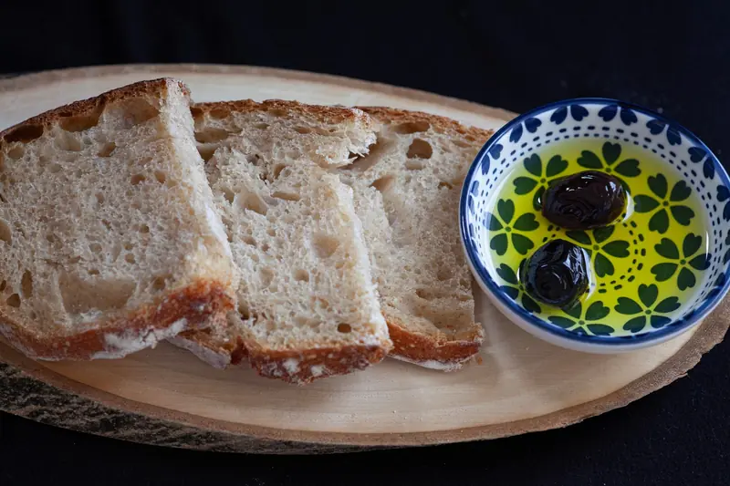 Slices of rustic bread with a dish of olive oil and olives on a wooden board