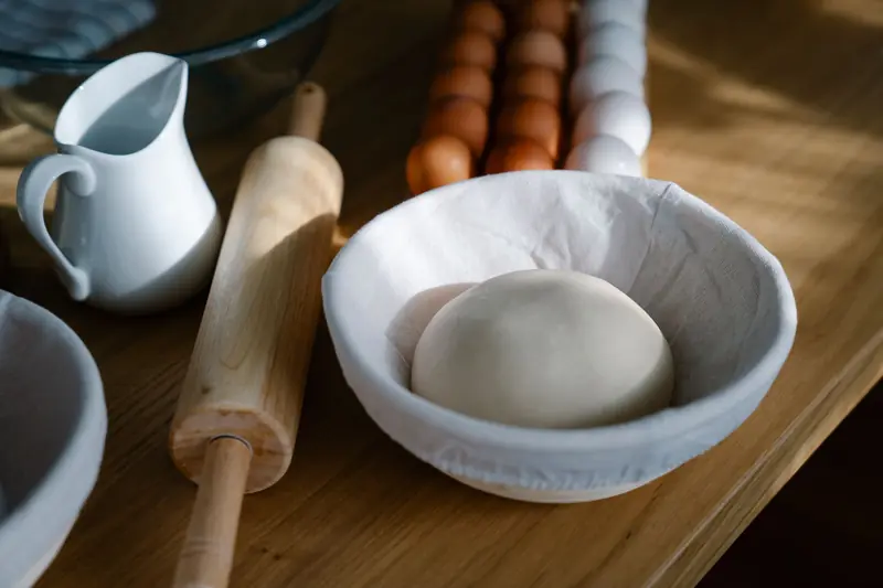 A bowl with dough near a rolling pin, jug, and eggs on a wooden table - perfect for baking themes