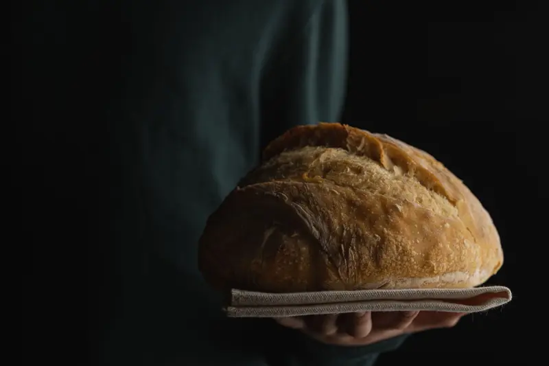 Close-up of a fresh baked loaf of bread held in hands with a dark background