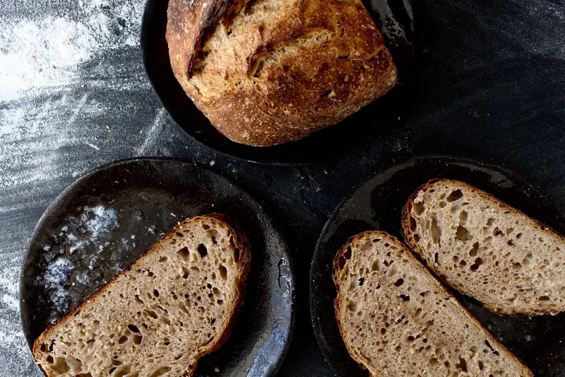 Freshly baked sourdough loaf and slices on dark plates with flour dusted surface
