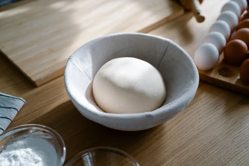 Fresh dough resting in a bowl with eggs and flour on a wooden kitchen counter, ideal for baking scenes