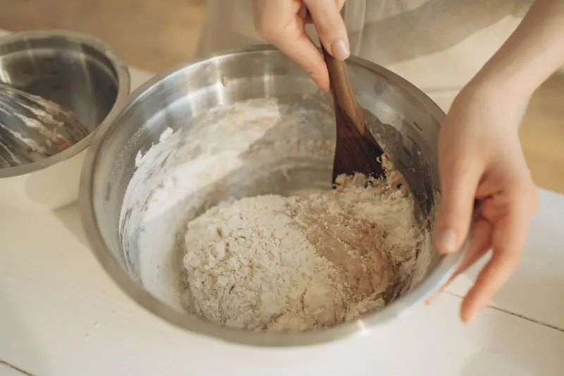 Hands mixing dough with a wooden spatula in a stainless steel bowl, perfect for baking themes
