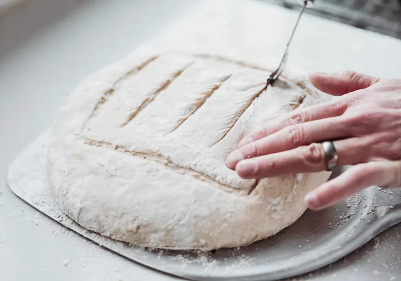 A detailed view of hands scoring bread dough for baking, showcasing artisanal bread preparation