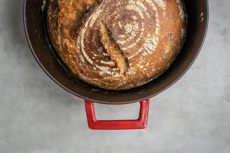 Freshly baked artisan bread in a red Dutch oven, showcasing rustic texture