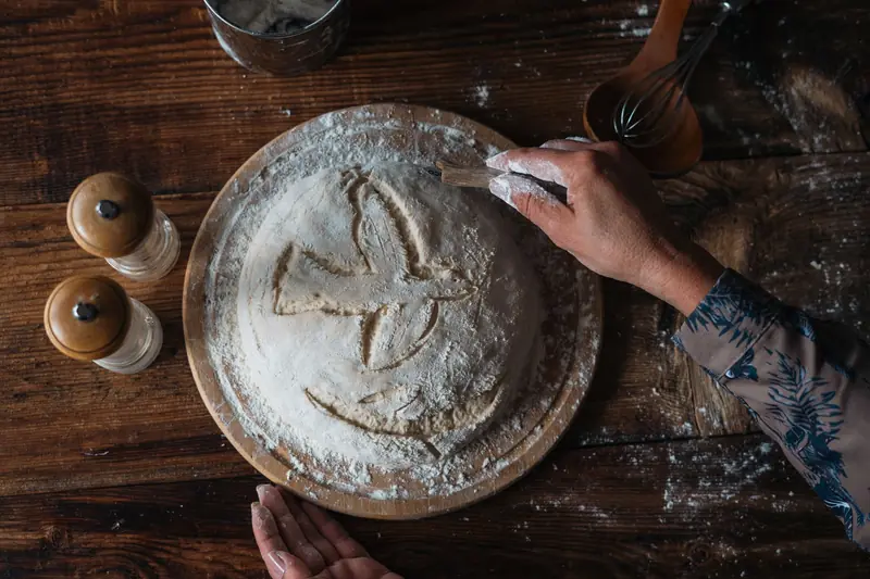 A person prepares rustic homemade bread dough with flour on a wooden table, creating a cozy atmosphere